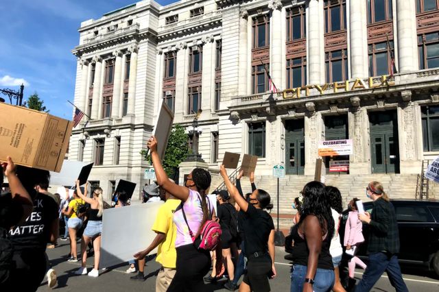 Protesters march in front of Newark City Hall, holding signs